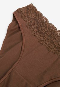 Brun linne med en texturerad spetskant längs halsringningen. Tyget är mjukt med en slät yta och synliga sömmar.