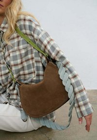 Hnedá semišová kabelka na rameno s oblým tvarom, vybavená zapleteným svetlomodrým remienkom a zeleným nastaviteľným koženým ramenným remienkom.