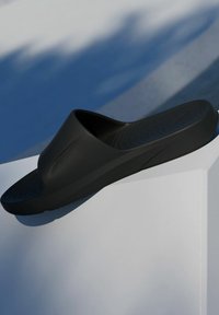 Black slide sandal with a textured footbed and a smooth, curved upper design. Made of soft, flexible material; minimalist, modern shape.