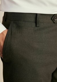 Pantalones de espiga verde oscuro con corte recto, bolsillos laterales y ajuste entallado. Cuenta con cierre de botón y una textura sutil.