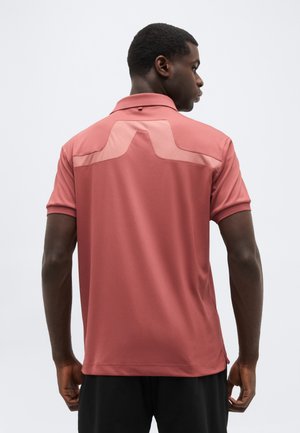 Uomo visto di spalle che indossa una polo a maniche corte color rosa antico con un distintivo dettaglio a yoke rosa più chiaro sulla parte superiore della schiena.