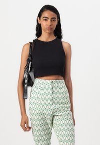 Svart rillede crop top kombinert med grønne og hvite mønstrede høytalede bukser, med bølgede linjer. Modellen holder en svart håndveske.