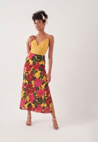 Geel mouwloos topje met V-hals, gecombineerd met een bloemen maxi rok met roze bloemen op een gele achtergrond en een zijsplit.
