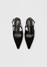 Fekete, hegyes orrú, pántos magassarkú cipő puha velúr külsővel, vékony bokapántokkal és párnázott talpbéléssel, belső oldalon logóval.