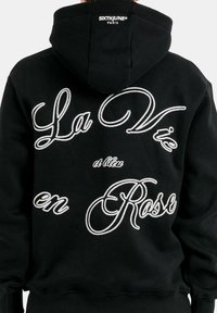 Felpa nera con cappuccio, caratterizzata da testo ricamato bianco "La Vie en Rose" e "et bleu" sul retro, dotata di cappuccio regolabile e polsini a coste.