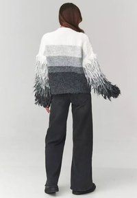Sweter dzianinowy w gradientowych odcieniach szarości, z frędzlami na rękawach. W połączeniu z czarnymi spodniami o szerokich nogawkach i czarnymi butami. Miękka faktura.