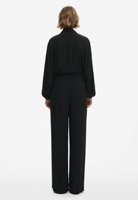 Chemise noire à manches longues avec un col, associée à un pantalon taille haute à jambes larges. Le tissu semble doux avec une texture lisse.