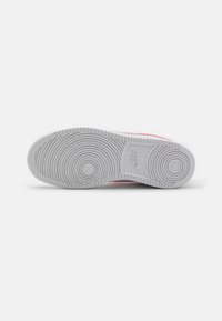 White sneaker sole with circular tread pattern, featuring a prominent logo and smooth texture. Accented with light pink details.