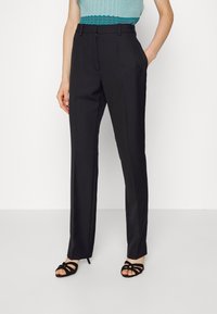 Czarne eleganckie spodnie z prostymi nogawkami, z bocznymi kieszeniami i gładką teksturą, stylizowane z jasnoniebieską bluzką i sandałami.