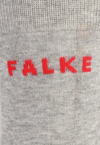 Calzino grigio lavorato a maglia con il nome del marchio "FALKE" ricamato in lettere di un rosso brillante. Texture liscia con un motivo a maglia uniforme.