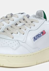 Sneaker in pelle bianca con lacci beige, dettagli perforati sulla punta e etichetta del logo AUTRY con una piccola bandiera americana.