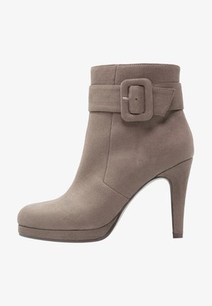 Botte cheville en cuir suédé taupe avec un talon haut, un large strap à boucle, un bout arrondi et une texture lisse. Design minimaliste avec des accents subtils.