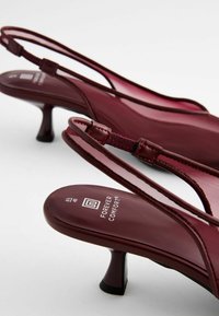Burgundy slingback-kengät, joissa on ohut hihna ja 4 cm korkea kartiomainen korko. Sileä nahkamainen materiaali ja pehmustettu pohja mukavuutta varten.