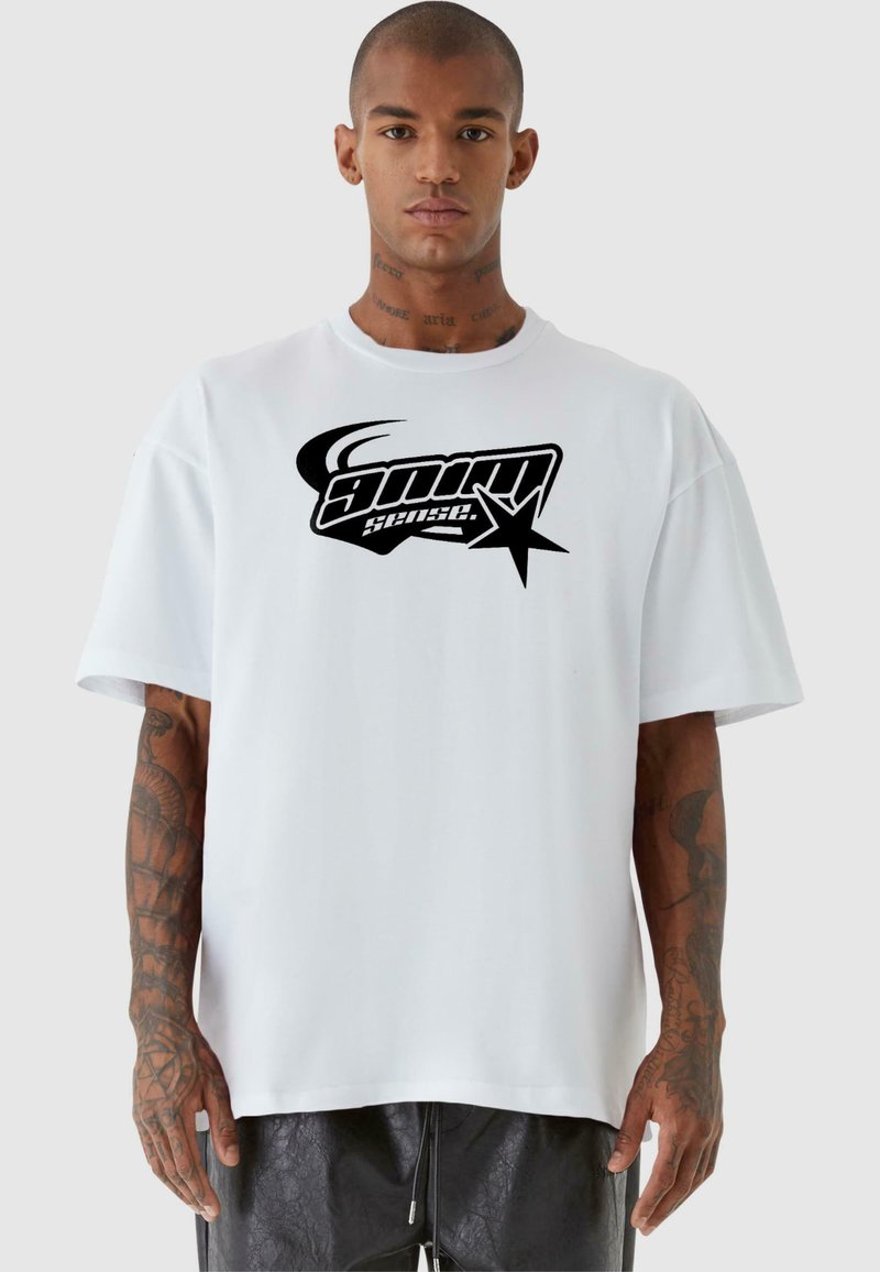 Hvit oversized t-skjorte med korte ermer, med et stort svart grafisk logo og stjerne-design i midten. Glatt bomullstekstur.