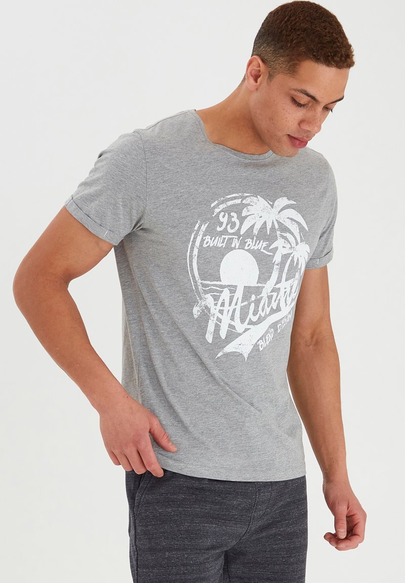 Camiseta de algodón gris de manga corta, con un diseño gráfico blanco de palmeras y sol. Cuello redondo, corte informal.