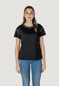 T-shirt nera a maniche corte con scollo rotondo e cuciture decorative grigio argento lungo le spalle, abbinata a jeans blu.