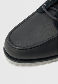 Must nahast king, millel on tekstuuriga ülemine osa, kontrastne hall kummist tald ning peened õmblused servadel lisakestvuse tagamiseks.