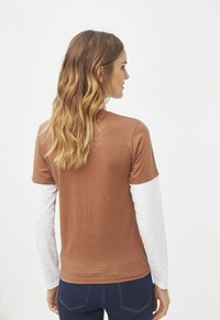 Camiseta marrón de manga corta superpuesta sobre una camiseta blanca de manga larga, con cuello redondo y tejido suave, vista desde la parte de atrás.