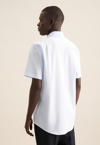 Camicia azzurra chiara a maniche corte con colletto a camicia, tessuto liscio e orlo curvo, indossata con pantaloni neri. Design semplice, senza motivi.