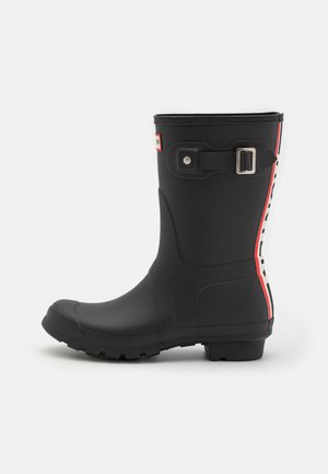 Bota de chuva preta de borracha com detalhe de fivela retangular e marcação em vermelho e branco ao longo do lado. Possui sola texturizada para tração.