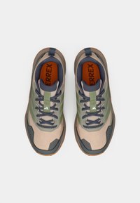 Μπεζ παπούτσια πεζοπορίας με πράσινες και μπλε ναυτικές λεπτομέρειες, υφή στην επάνω επιφάνεια, λαστιχένια σόλα και αντίθετη πορτοκαλί εσωτερική σόλα. Διαθέτουν κορδόνια και ενισχυμένη μύτη.