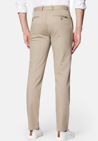 Beige bavlněné kalhoty se zadními kapsami, rovný střih a jemné švy. Nosit s bílými teniskami.