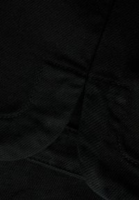 Detailný záber na čiernu látku s viditeľným diagonálnym vzorom tkania a prešitými švami vytvárajúcimi preloženú, vrstvenú textúru.