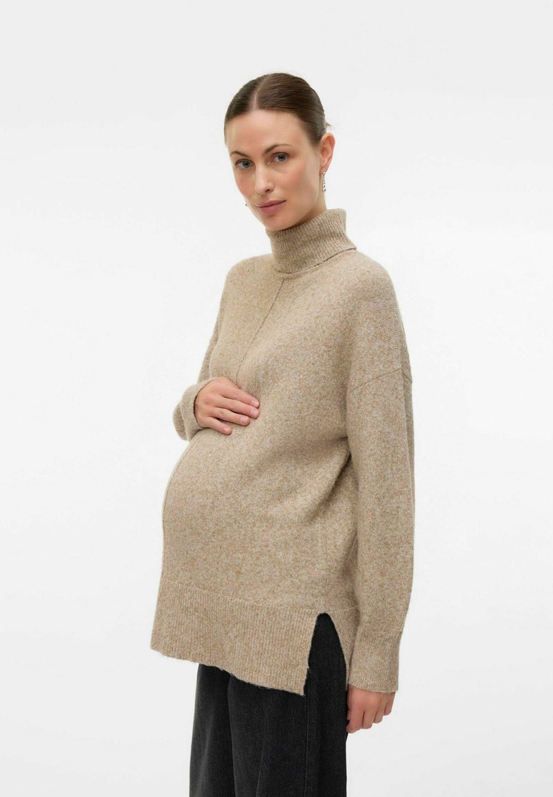 Pletena bež turtleneck sweater sa opuštenim krojem, bočnim prorezima i rebrastim manžetama, nosi se preko crnih hlača, ističući stil za trudnice.