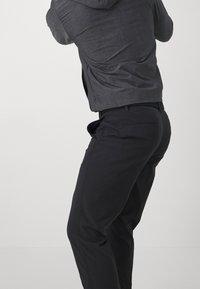 Šedá mikina s texturovanou tkaninou a stažitelnou kapucí, nošená s černými kalhotami s rovné střihy a kapsami.