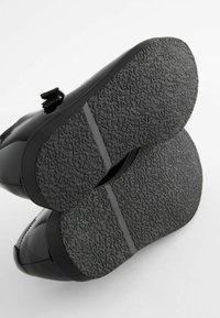 Zapatos de charol negro con suela de goma texturizada, que presentan una punta redondeada y acentos mínimos. Adecuados para diversas ocasiones.