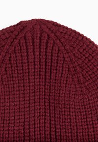 Burgundy knitted beanie with vertical ribbed texture and a rounded crown, made from a soft, chunky yarn for warmth.
