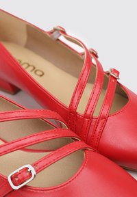 Zapatos de piel rojos de tacón bajo con correas cruzadas, que presentan un detalle de hebilla. Textura suave y diseño de punta redondeada.