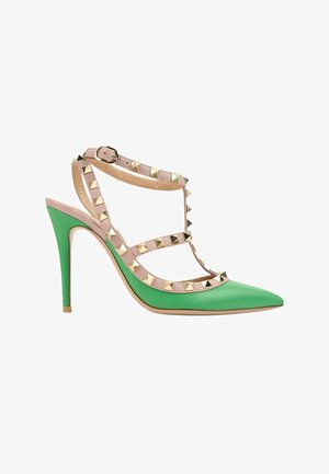 Chaussure à talon haut pointue verte avec des brides cloutées beige et une fermeture à boucle latérale.