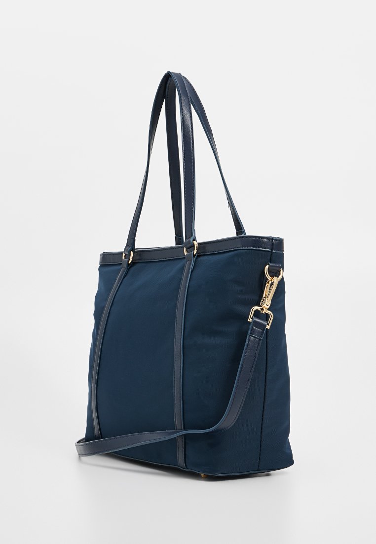 Sac fourre-tout bleu marine en tissu texturé avec des accessoires en or. Doté de deux longues poignées et d'une bandoulière réglable.