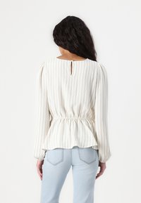 Blouse blanche à rayures avec des manches bouffantes, taille cintrée et détail en trou de serrure à l'arrière. Associée à un denim bleu clair.