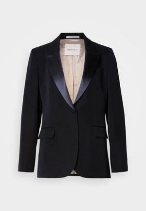 Sacou negru cu rever din satin, închidere cu un buton, două buzunare frontale și căptușeală bej. Eticheta spune „GANT.” Design clasic, croit cu măiestrie.