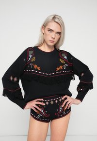 Μαύρο πλεκτό πουλόβερ με περιθώρια και πολύχρωμη κεντητική διακόσμηση, σε συνδυασμό με κοντές παντελόνες που διαθέτουν διακοσμητικό μοτίβο και τελείωμα.