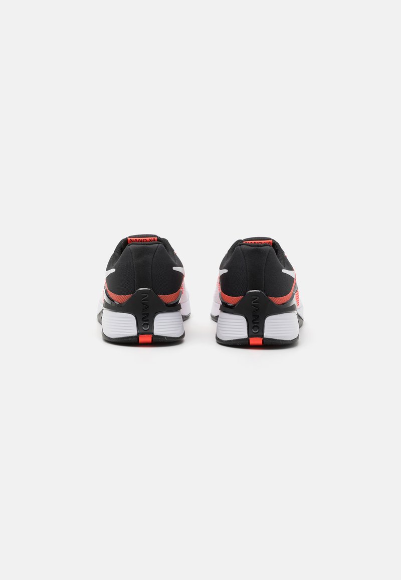 Zapatillas deportivas en blanco y negro con detalles en rojo. Presentan un talón acolchado, tela texturizada y una suela de goma resistente.