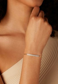 Bracelet en métal avec une bande dorée élégante et une barre argentée ornée de cristaux transparents, présentant un design moderne et minimaliste.