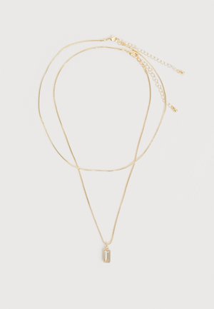 Dve jemné zlaté retiazky na krk, jedna s malým obdĺžnikovým priehľadným drahokamovým príveskom, položené na bielom pozadí.