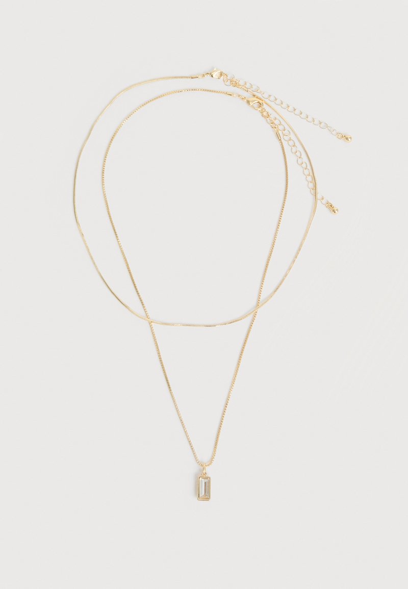 Δύο λεπτές χρυσές αλυσίδες για κολιέ, η μία με ένα μικρό ορθογώνιο διαυγές πέτρινο μενταγιόν, τοποθετημένες επίπεδα σε λευκό φόντο.