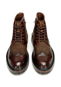 Brązowe skórzane i zamszowe botki za kostkę z detalami w stylu brogue, okrągłym noskiem, sznurowaniem i zamkiem błyskawicznym oraz kontrastującą czarną gumową podeszwą.