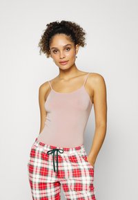 Top de alças spaghetti rosa claro e calças de pijama xadrez vermelhas com cordão verde, apresentando uma textura suave e um design ajustado.