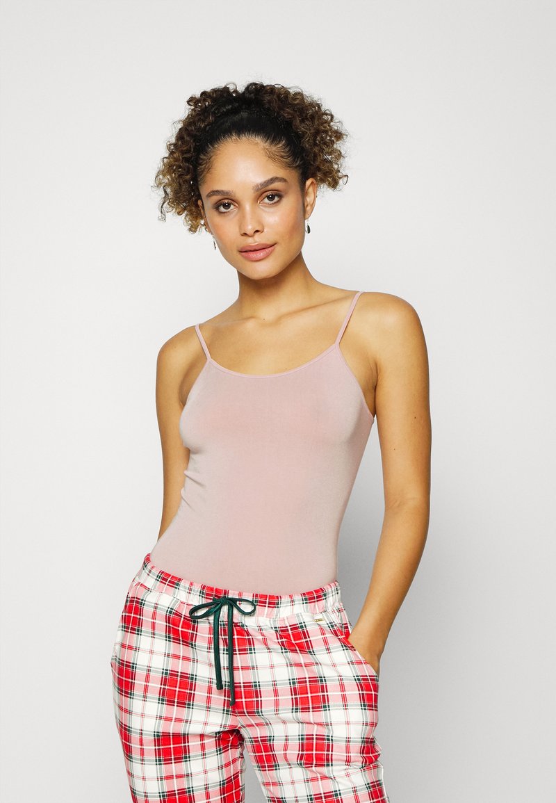 Top de alças spaghetti rosa claro e calças de pijama xadrez vermelhas com cordão verde, apresentando uma textura suave e um design ajustado.