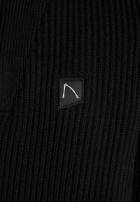 Schwarzer, gestrickter Pullover mit geripptem Muster, der auf der oberen linken Seite einen kleinen schwarzen Patch mit einem weißen Design aufweist.