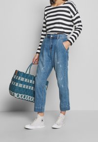 Randig svart och vit långärmad topp, högmidjade ljusblå denimbyxor med fickor, grå högsneakers och en vävd teal-väska.