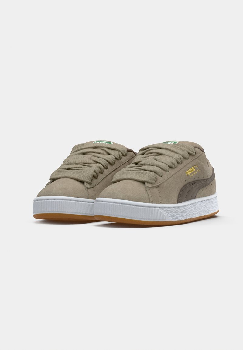 Zapatillas de ante beige con suelas de goma blanca, con punteras redondeadas, cordones planos y una franja de acento marrón en el lateral. Detalle del logotipo en dorado incluido.