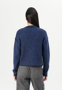 Maglione blu a coste con maniche lunghe, caratterizzato da un collo rotondo e una trama a contrasto. Abbinato a pantaloni cargo grigi con tasche.