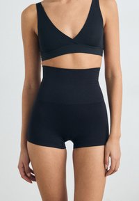 Crna bešavna bralette s V-izrezom i visokim hlačicama. Ovaj set sadrži glatku tkaninu i prilagođeni kroj.