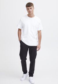 Tricou alb din bumbac, cu mâneci scurte, asortat cu pantaloni negri. Modelul poartă adidași albi. Design simplu, fără logo-uri sau modele vizibile.
